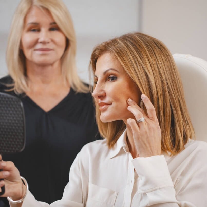 Patient examining her skin with a mirror while another woman watches